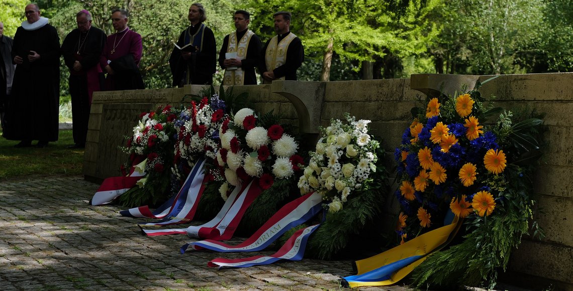 Blick auf die Internationale Kriegsgräberstätte mit Vertretern verschiedener Konfessionen im Hintergrund