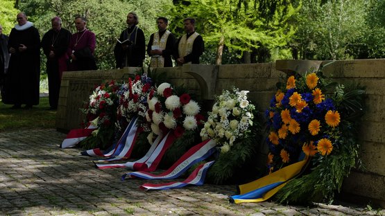 Blick auf die Internationale Kriegsgräberstätte mit Vertretern verschiedener Konfessionen im Hintergrund